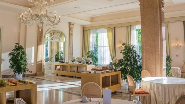 Un hall d’hôtel spacieux, agrémenté d’un lustre, de grandes fenêtres et d’un comptoir d’accueil.