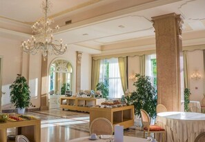 Een ruime hotellobby met een kroonluchter, grote ramen en een receptiebalie.