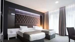 Une chambre d’hôtel moderne avec un grand lit, deux petits lits, une table de chevet et une chaise.