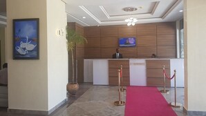 Un espace d’accueil avec un comptoir de réception en bois, un téléviseur et un tapis rouge menant au comptoir.