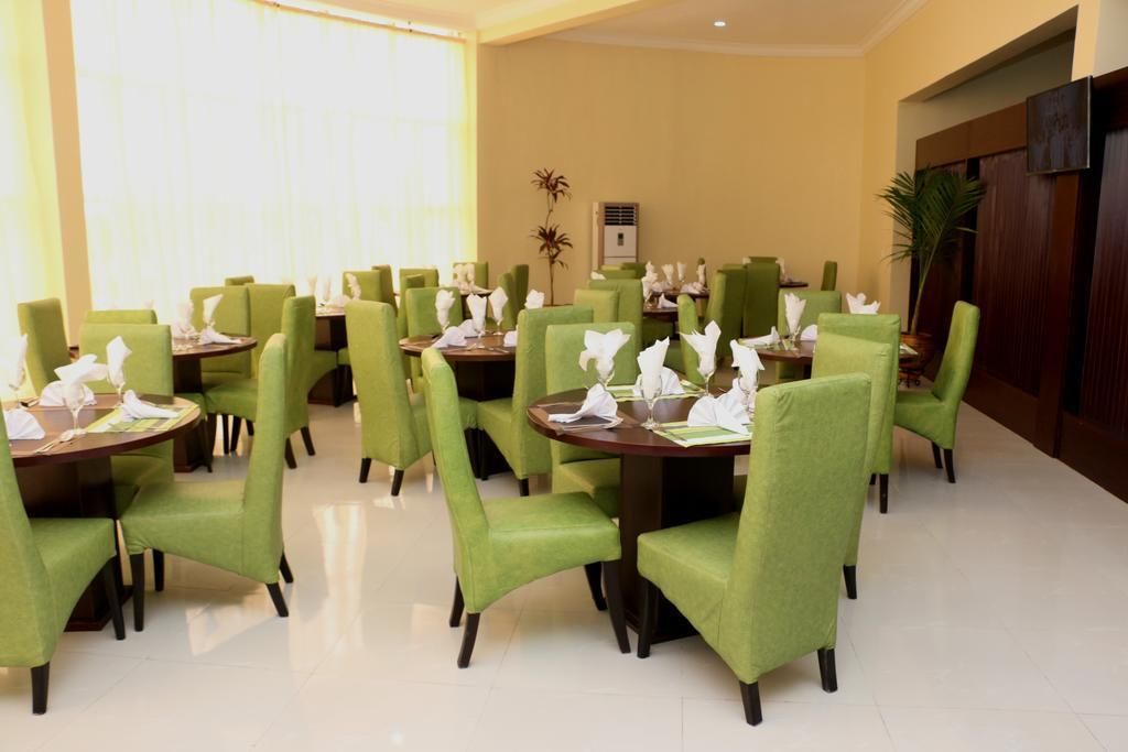 A dining area with round tables and green upholstered chairs, arranged in a spacious layout.