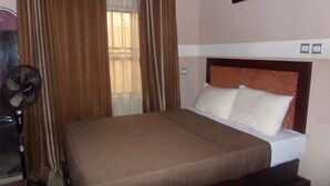 Ein Schlafzimmer mit Bett, Vorhängen, einem Standventilator und einem Wandbild.
