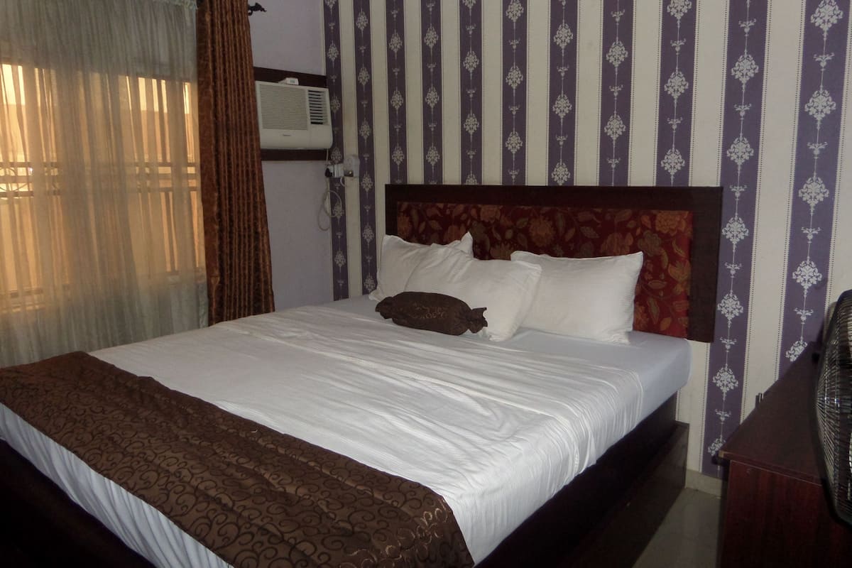 A neatly made bed with a patterned bedspread, a headboard with a floral design, and a wall air conditioner.