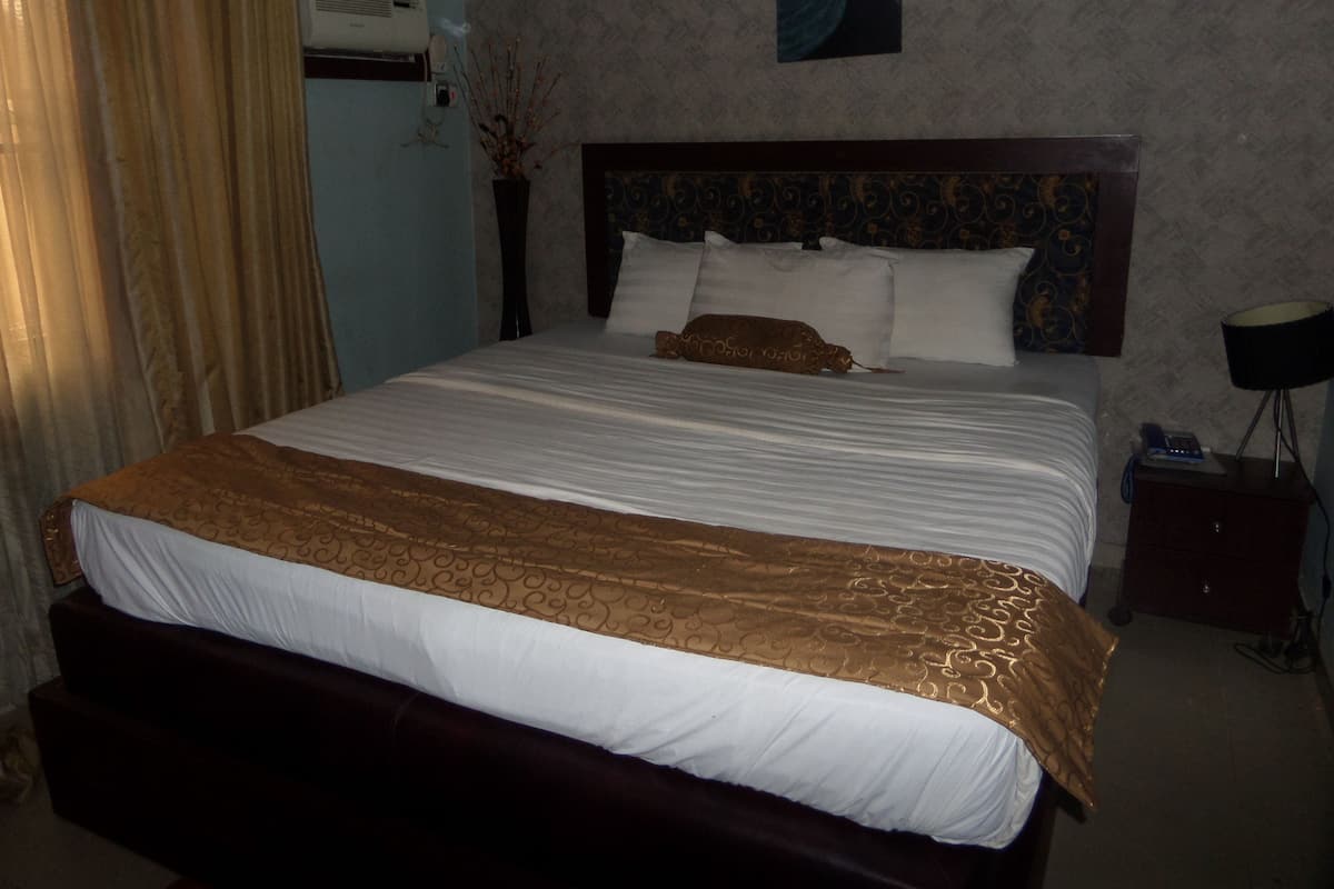 A hotel room with a large bed, a bedside table, a lamp, and a wall-mounted air conditioner.