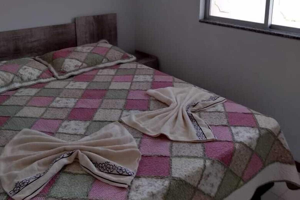 A bedroom with a bed, two windows, and an air conditioning unit.