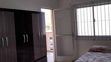 Un dormitorio con cama, armario y ventana con barrotes.