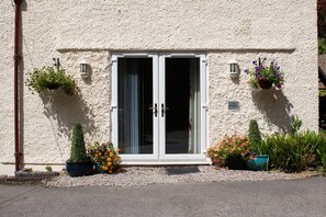 A building with a textured facade, a set of double doors, and potted plants with flowers. - The Coachhouse (Colwyn Bay)