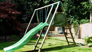 A wooden swing set with a green slide in a backyard. - The Coachhouse (Colwyn Bay)