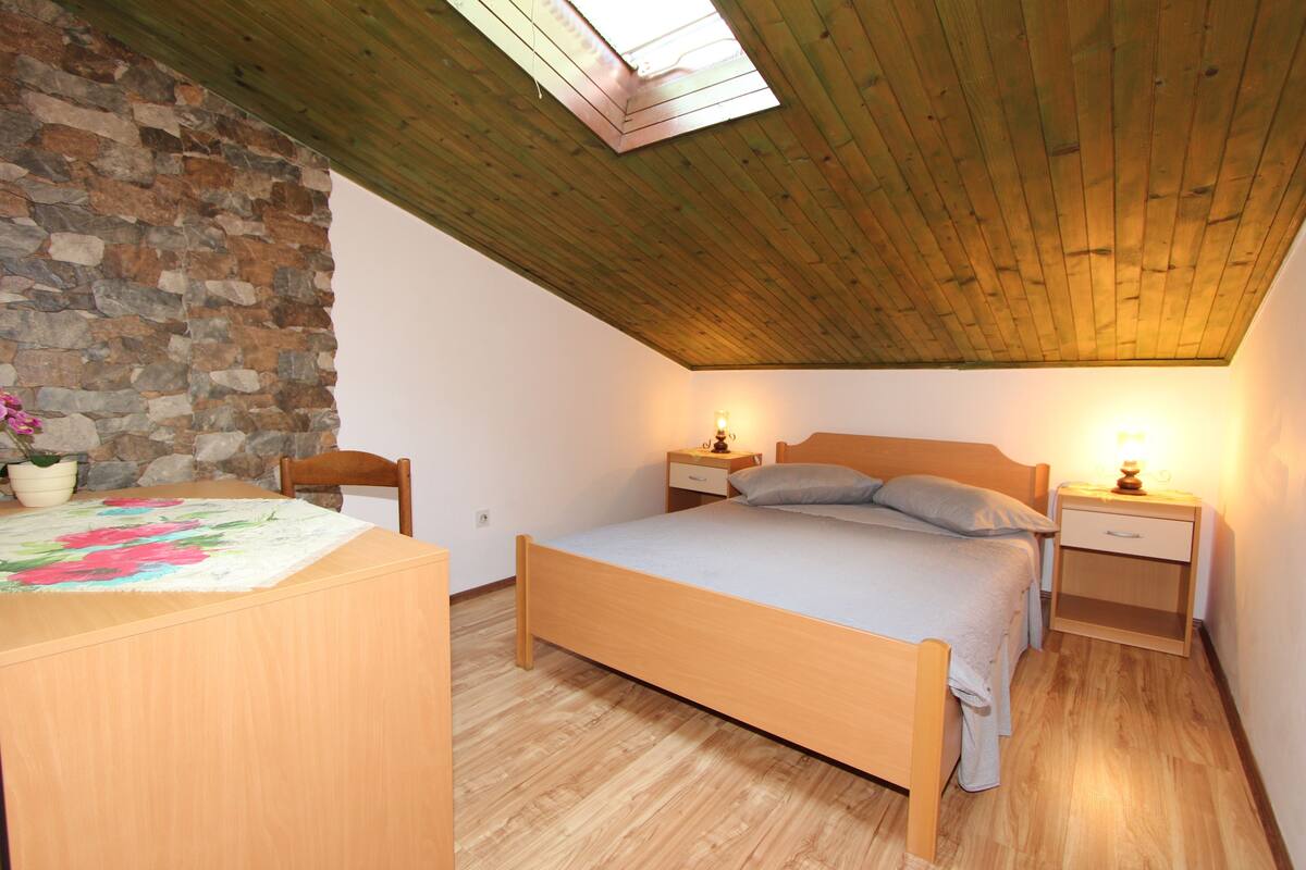Ein Schlafzimmer mit Holzboden, einer Steinwand, einem Bett, Nachttischen und einem Beistelltisch.