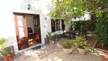 Un patio con puerta de madera, plantas en macetas, piso de baldosas hexagonales y una mesa con sillas.