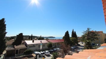 Vista de un pueblo costero con edificios, coches aparcados y un cielo azul despejado.