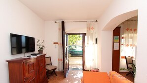 Sala de estar com televisão, armário de madeira, sofá e vista para um carro através de uma porta aberta.