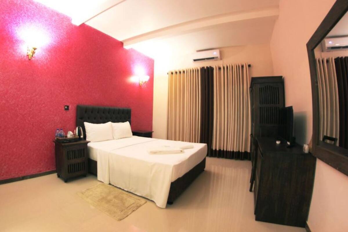 Een hotelkamer met een bed, nachtkastje, dressoir, spiegel en een raam met gordijnen.