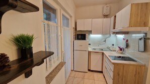 A compact kitchen with white cabinets, a built-in microwave, a refrigerator, and a sink. - Apartments Godena (Rovinj)
