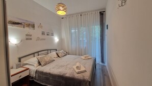 A bedroom with a bed, bedside tables, a wall-mounted shelf, and a window with curtains. - Apartments Godena (Rovinj)