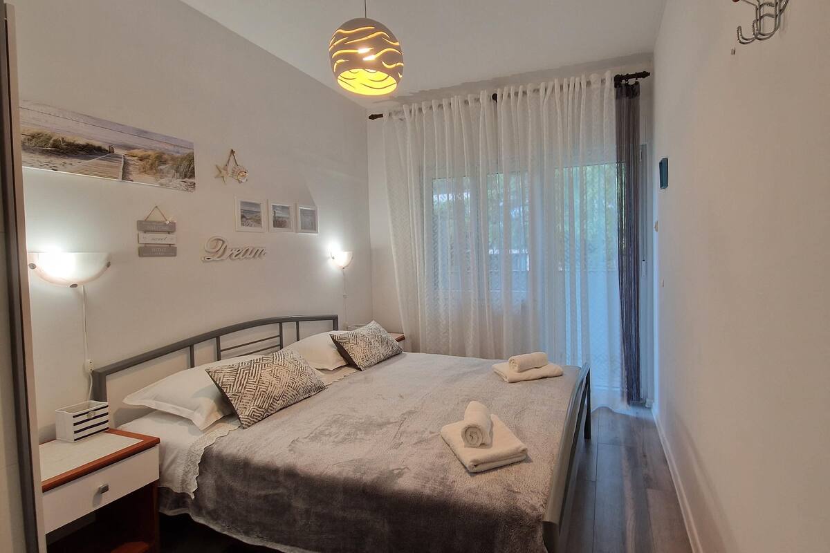 A bedroom with a bed, bedside tables, a wall-mounted shelf, and a window with curtains.