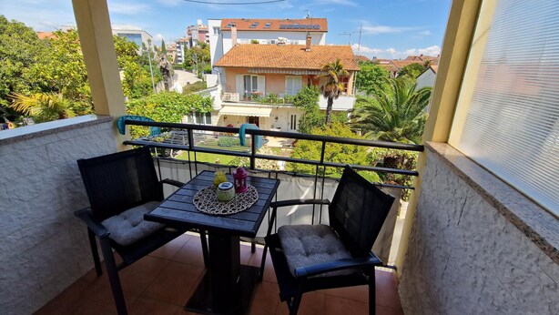 A balcony with a table and two chairs, overlooking a residential area with houses and greenery. - Apartments Godena (Rovinj)