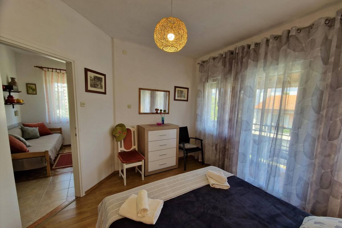 A bedroom with a bed, a dresser, a chair, a desk, a mirror, and a hanging light fixture.