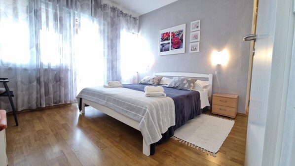 Un dormitorio con cama, mesitas de noche, una lámpara y una ventana con cortinas.
