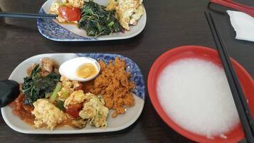 Two plates of food with chopsticks and a bowl of white substance, likely rice, on a table.