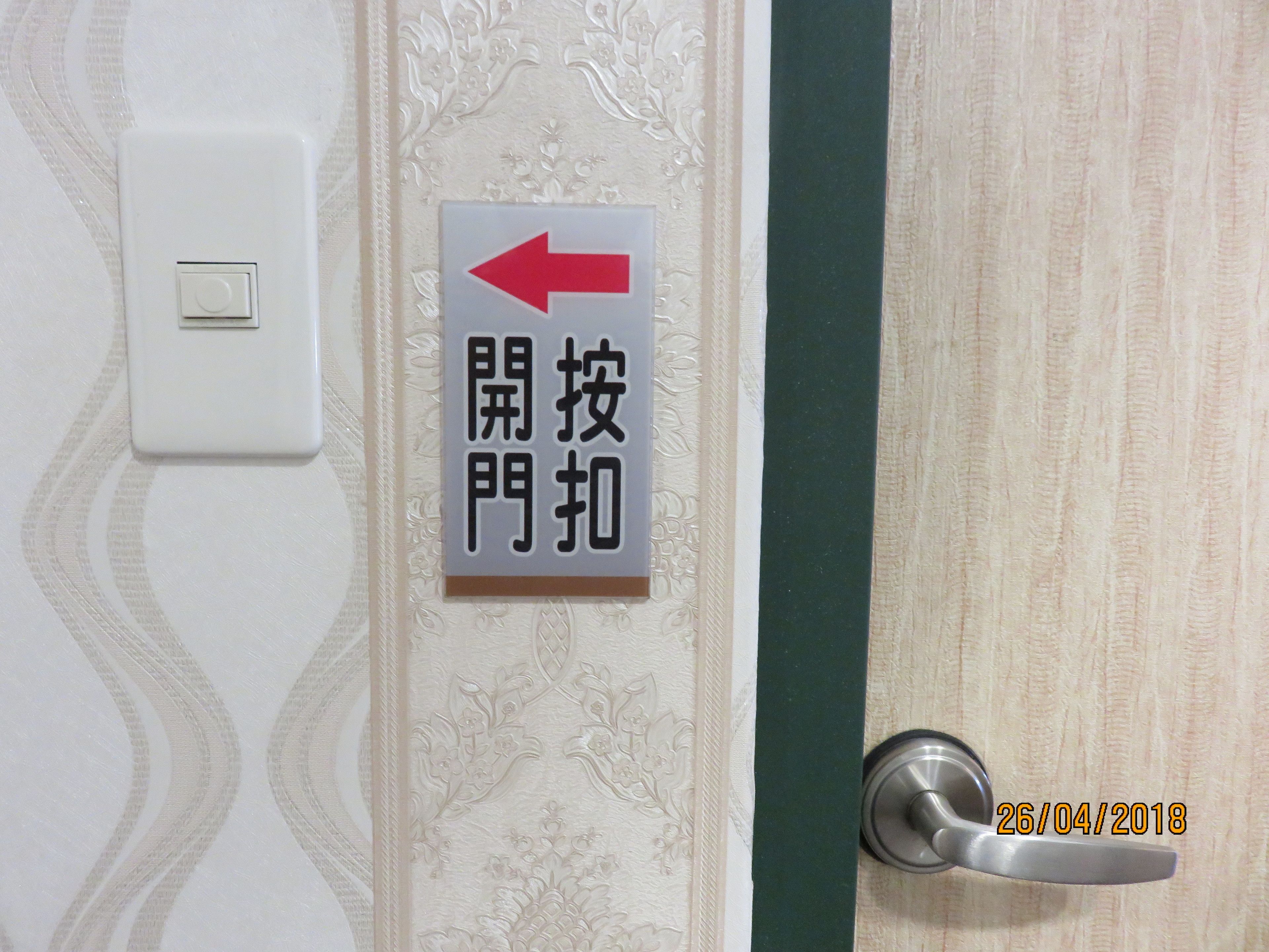 A door with a sign indicating the door opens to the left, a light switch, and a date stamp.