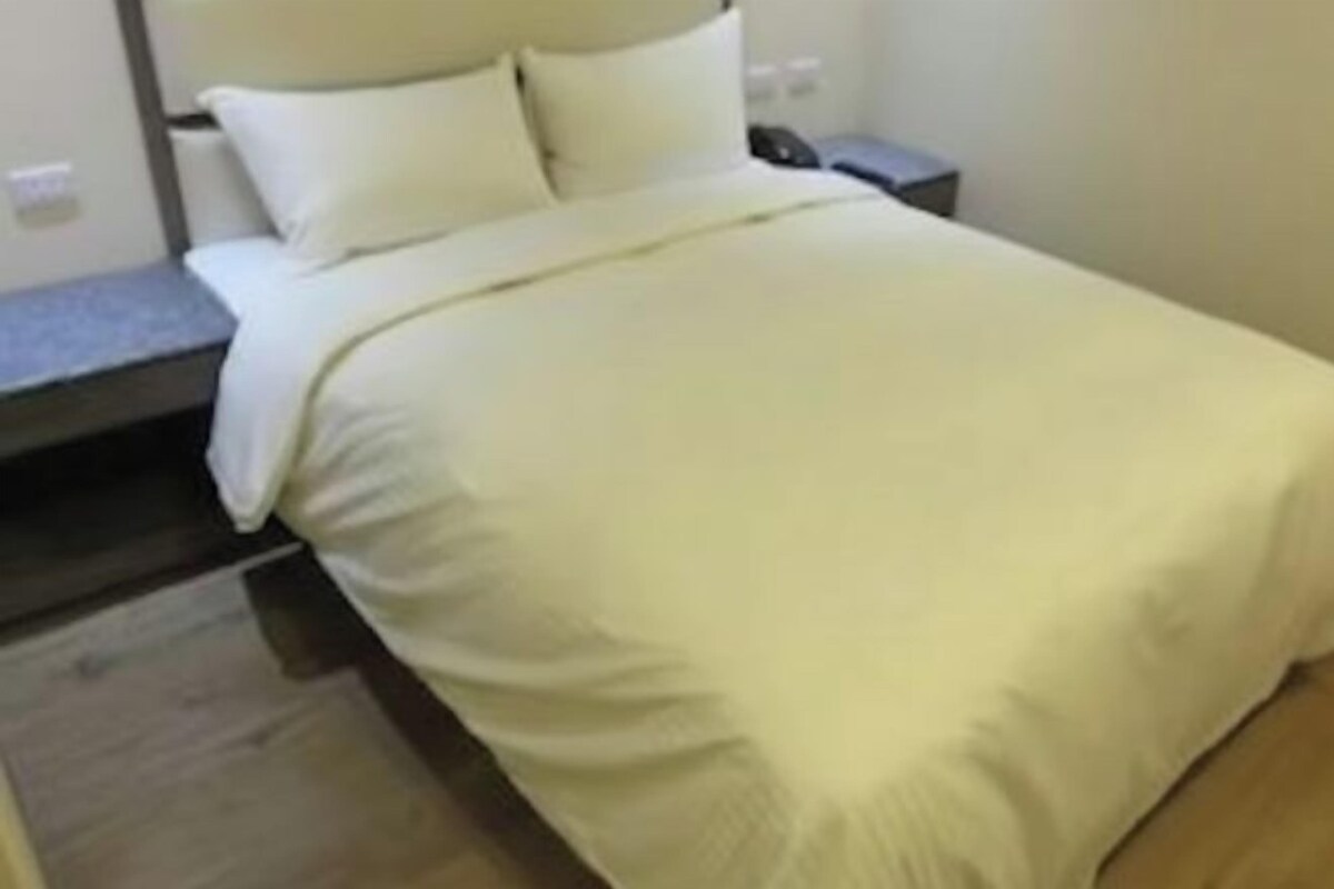 Un lit bien fait, avec une couette blanche et des oreillers, une table de chevet avec une lampe et un plancher en bois.