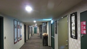 Un couloir avec des tableaux encadrés accrochés aux murs, une horloge et une porte avec une pancarte.