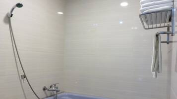 Un baño con bañera, cabezal de ducha y toallero con toallas.