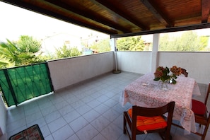 A covered balcony with a table set for two, featuring a floral tablecloth and a vase with flowers.