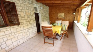 Eine Terrasse mit Steinsäulen, einem Holztisch und -stühlen, einem Fliesenboden und einer Holzdachkonstruktion.