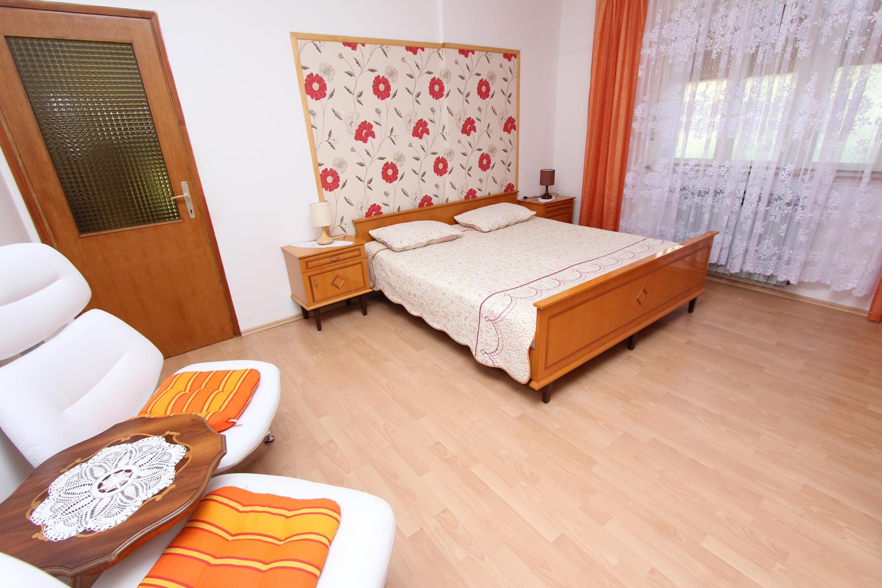 A bedroom with a wooden bed, a nightstand, a bedside table, a chair, and a door with a glass panel.