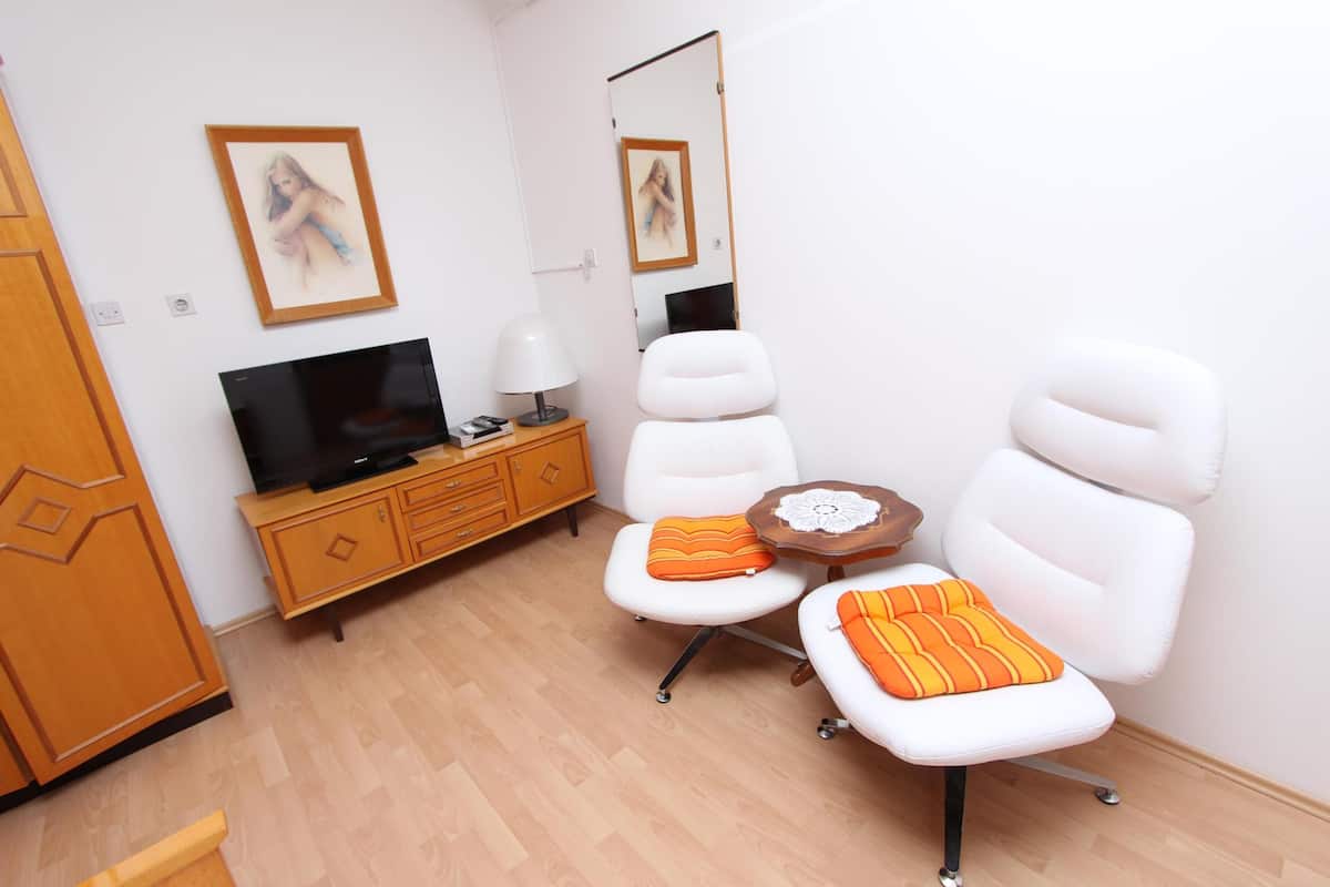 A modern living room with a flat-screen TV, white chairs, a wooden cabinet, and a small table with a lamp.
