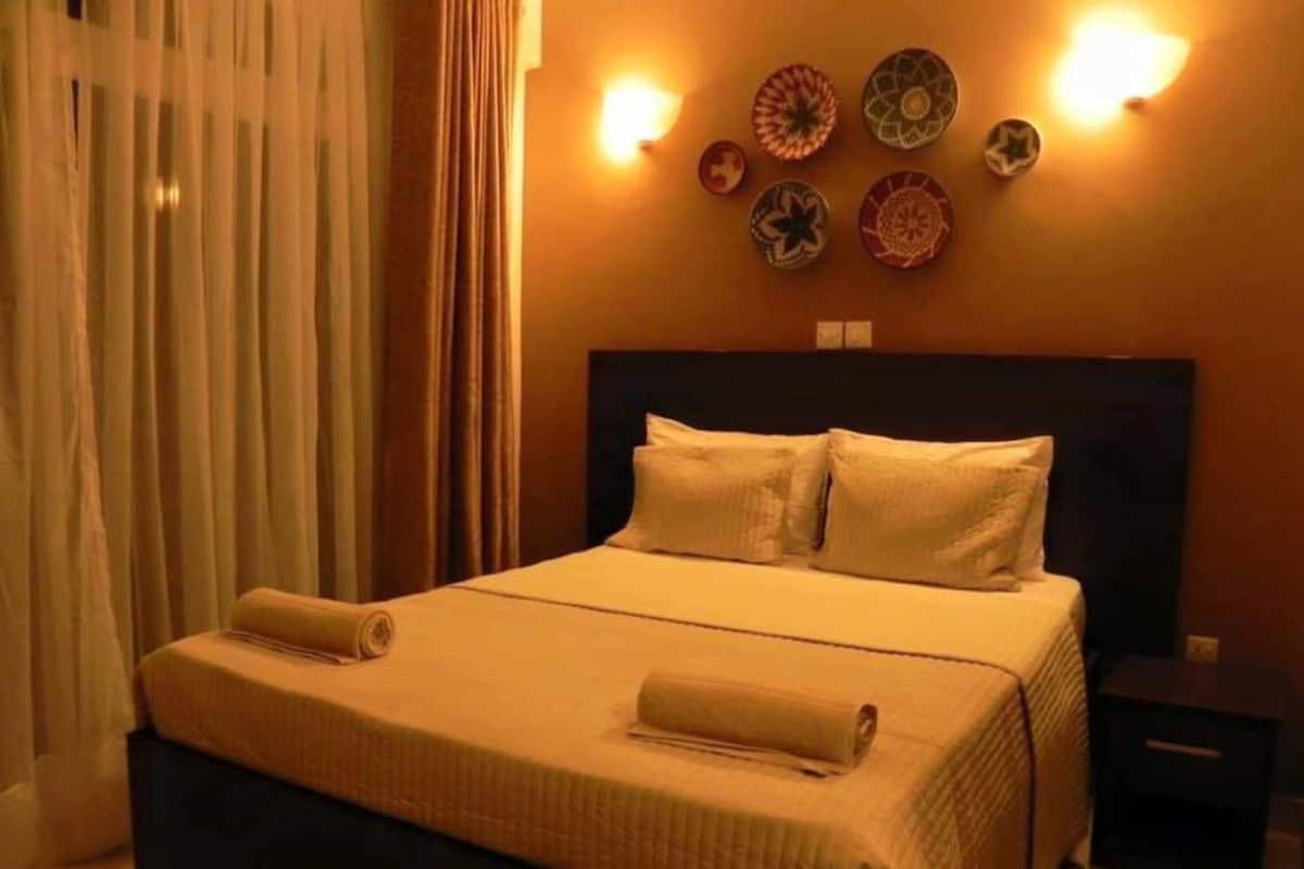 Una cama bien tendida con almohadas y una toalla enrollada, una mesita de noche y platos decorativos en la pared.