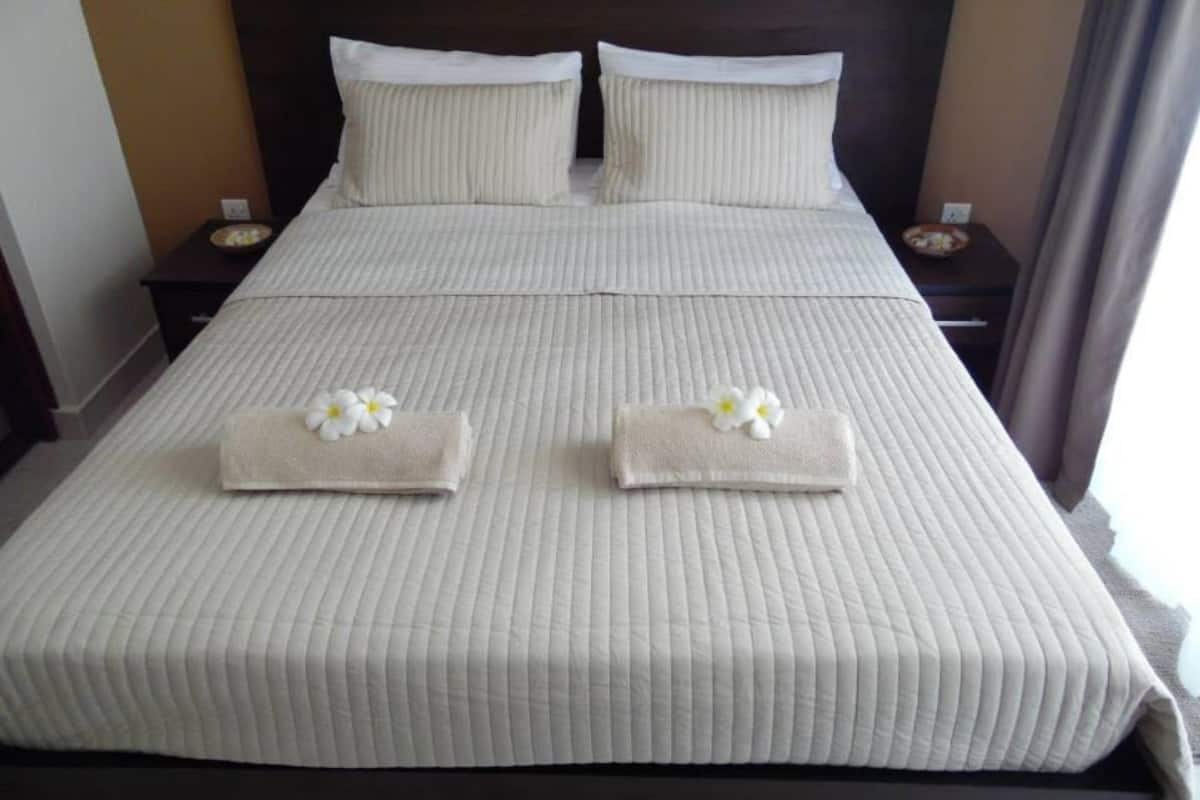 Una cama bien hecha con una colcha a rayas, dos almohadas y dos toallas con flores sobre un cabecero de madera.