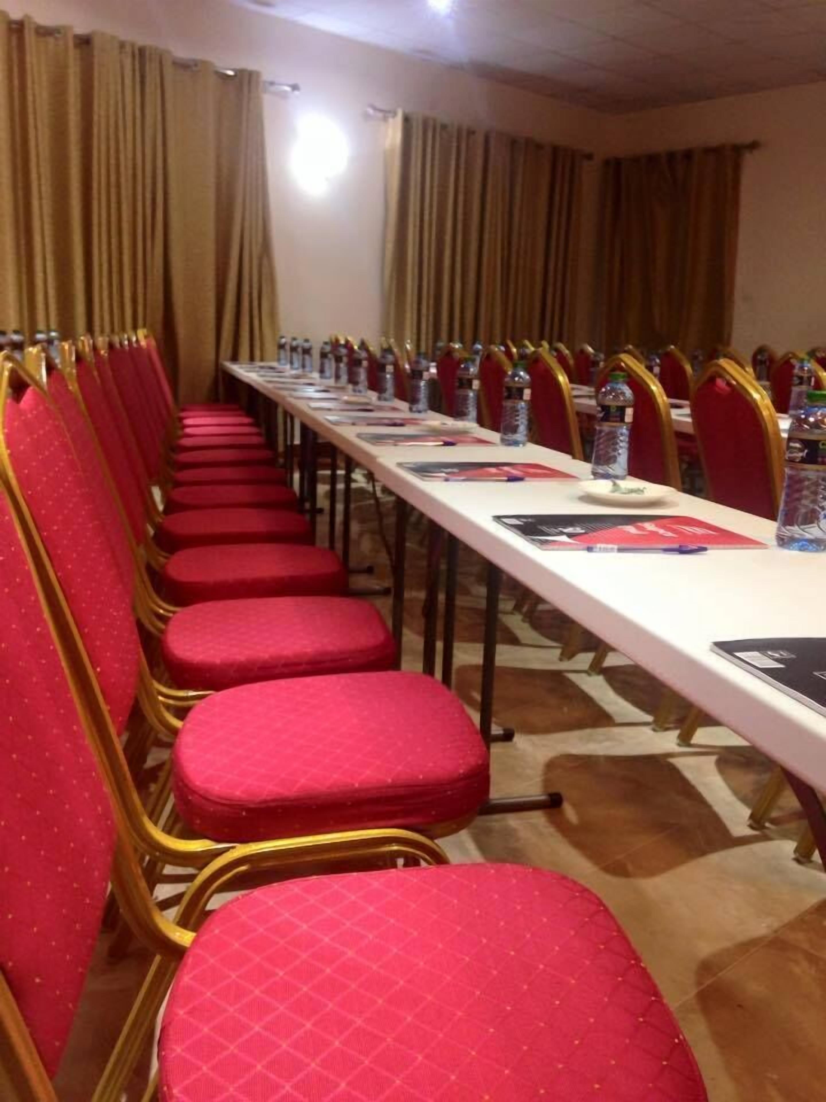 Une salle de conférence avec une longue table, des chaises rouges et des bouteilles d’eau.