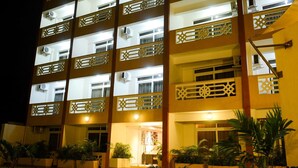 Un hotel de varios pisos con balcones, unidades de aire acondicionado y una entrada bien iluminada.
