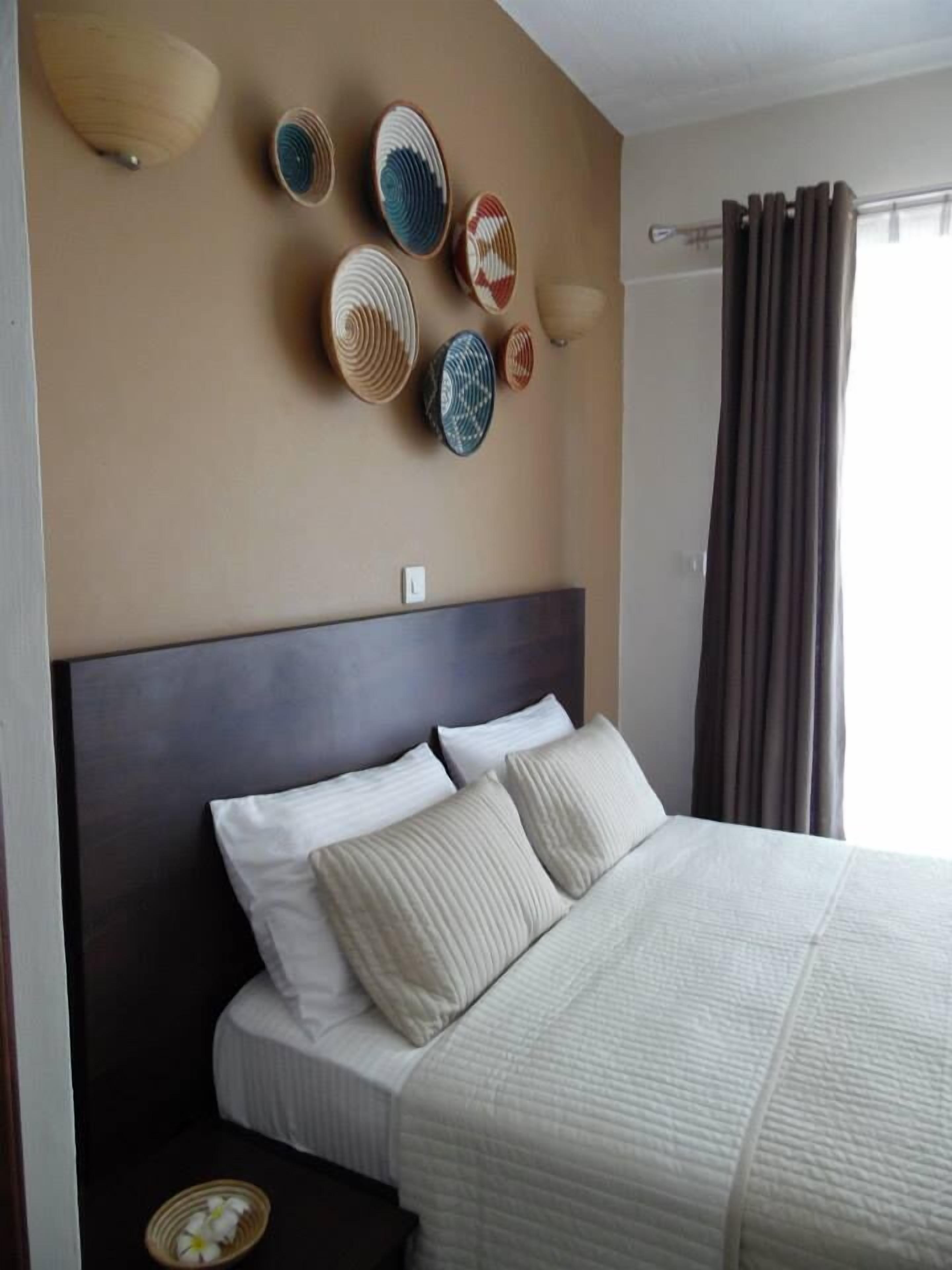 A neatly made bed with white bedding, a dark headboard, and a wall decorated with woven baskets.