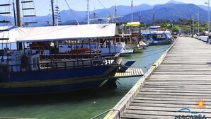 Un muelle con barcos, un espigón de madera y montañas al fondo.