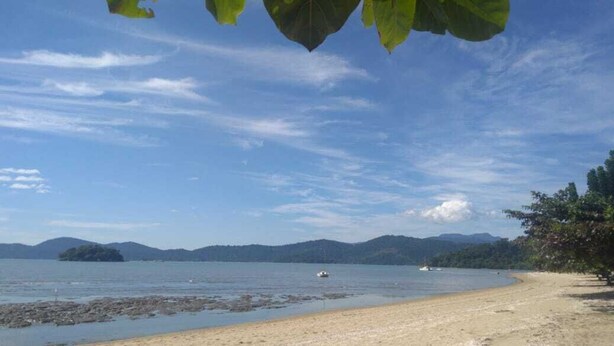 Una playa con cielo despejado, agua tranquila y montañas a lo lejos.