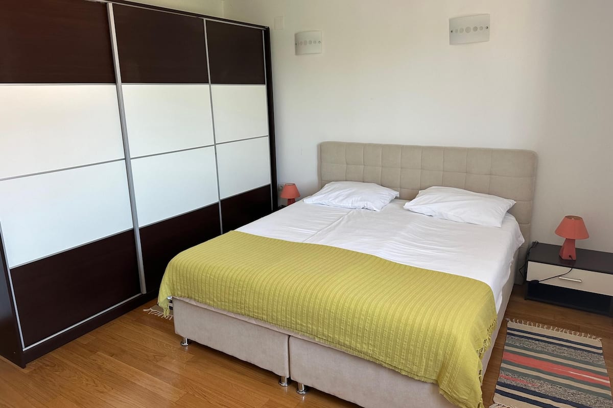 A bedroom with a bed, a wardrobe, a nightstand, and a lamp.