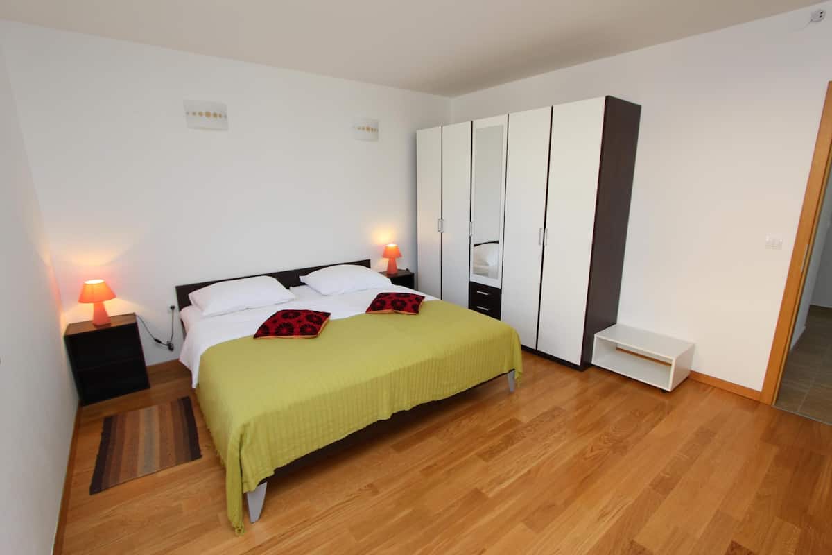A bedroom with a bed, bedside lamps, a wardrobe, and a small bench.