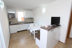 Une cuisine moderne avec des meubles blancs, une table à manger et un téléviseur posé sur un comptoir en bois.