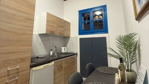 A compact kitchen with wooden cabinets, a blue cabinet with glass doors, a dining table with a placemat, and a potted plant. - Occasus Room (Halki)