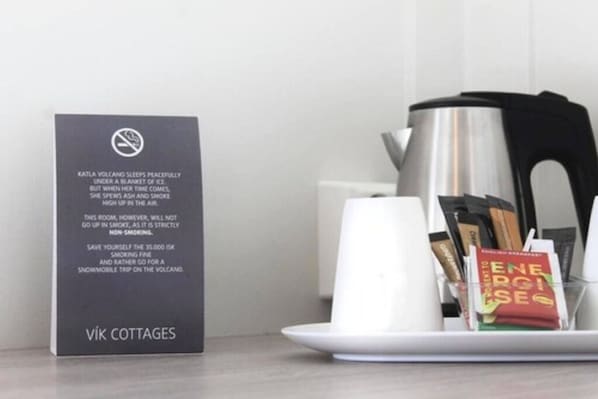A sign with a volcano theme, a white mug, a kettle, and a tray with books. - Vík Cottages (Vik I Myrdal)