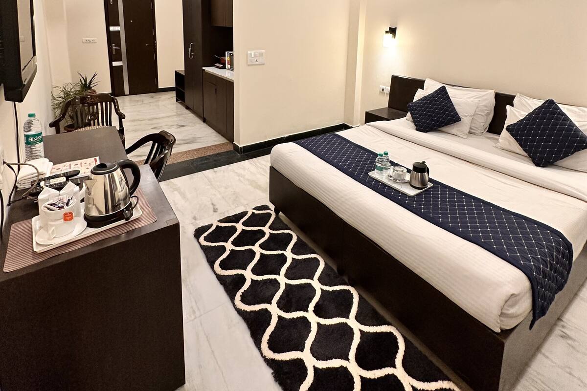 A hotel room with a bed, bedside table, and a desk with a kettle and cups.