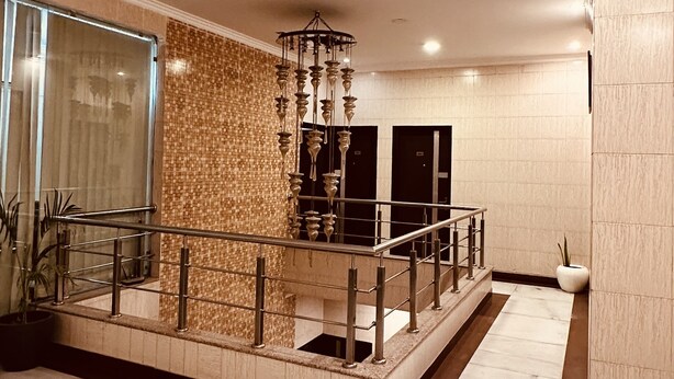 A spacious lobby with a marble floor, a decorative wall, a modern chandelier, and a glass railing. - Hollyhocks Residency (Gurugram)