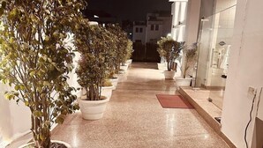 A corridor lined with potted plants leading to a building entrance. - Hollyhocks Residency (Gurugram)
