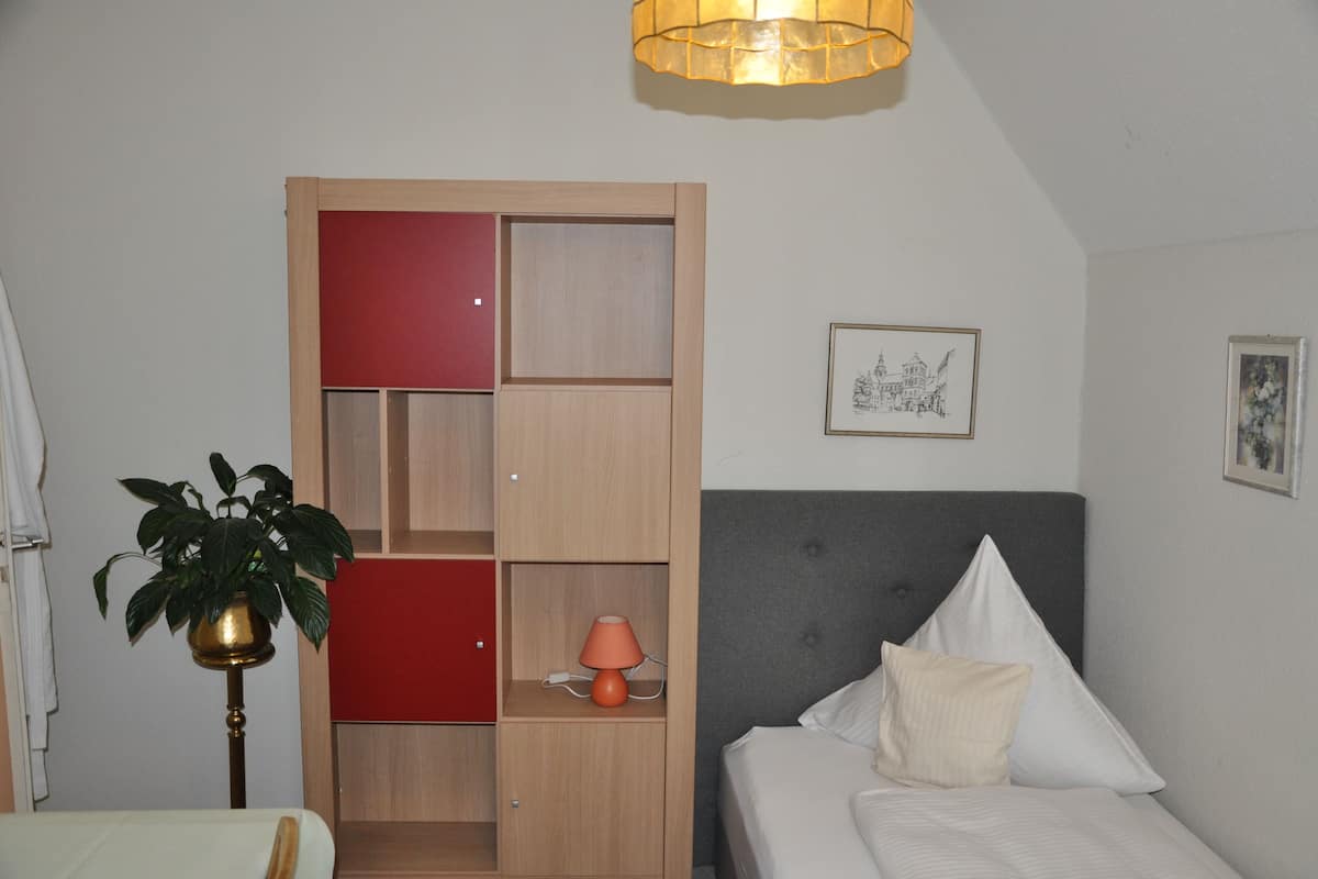 A bedroom with a bed, a bedside table, a lamp, a plant, and a wardrobe.