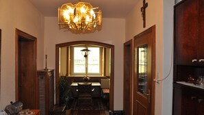 Un couloir agrémenté d’un lustre, de portes en bois, d’un banc et d’une fenêtre laissant entrer la lumière naturelle.