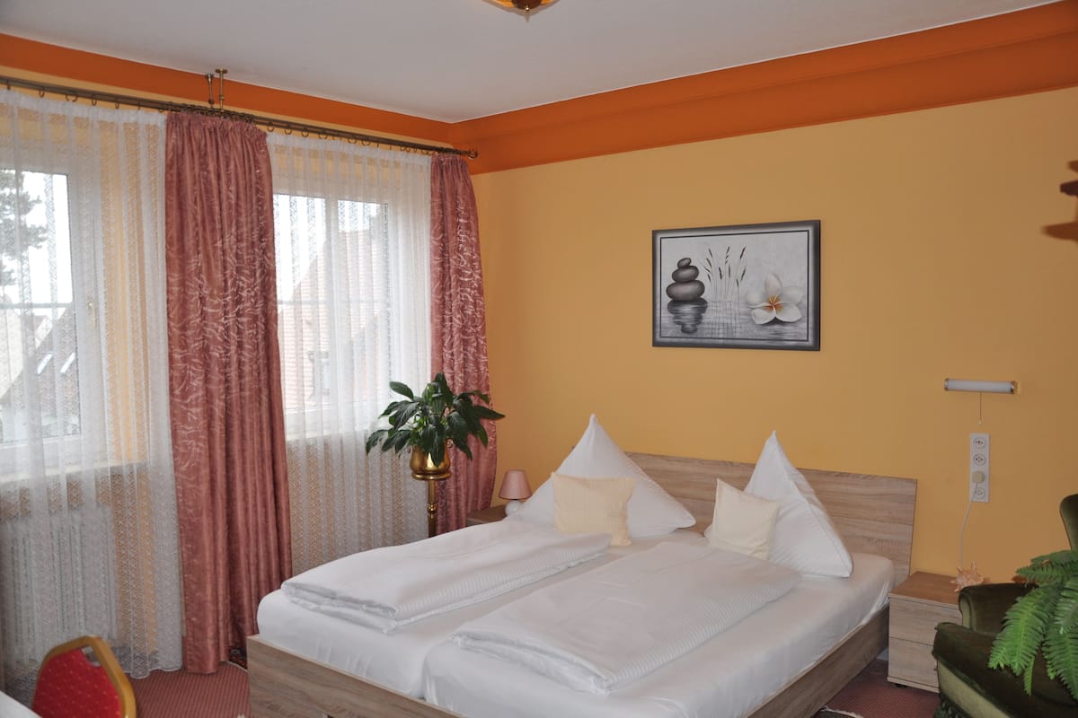 A hotel room with a bed, curtains, a wall-mounted picture, a bedside lamp, and a nightstand.